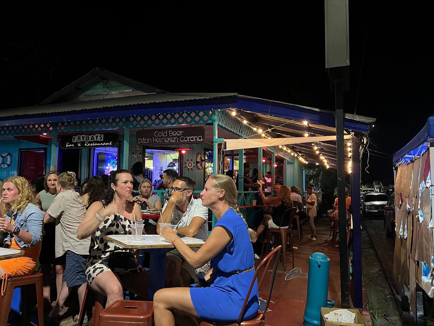 People dining and drinking at an outdoor, string-lit patio bar at night