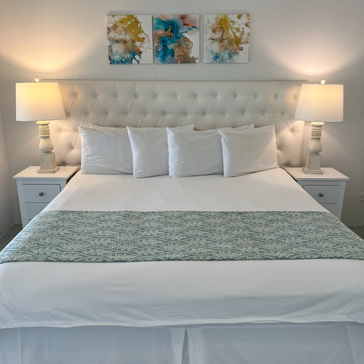 A bedroom with a bed lamps and three paintings on the wall