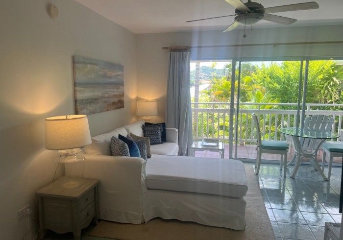 Bright bedroom with white daybed, lamp, balcony, and tropical greenery outside.