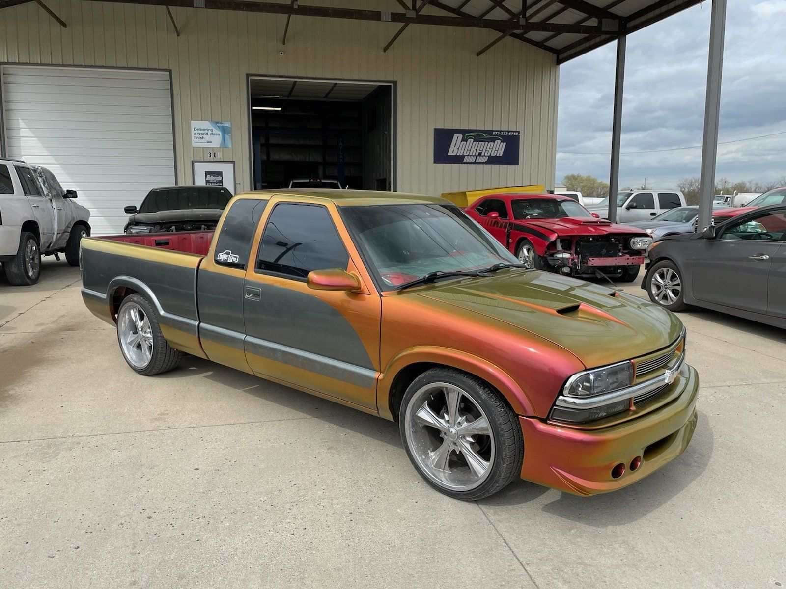 A custom S10 extended cab pickup truck with a color-shifting orange and green paint job parked in a shop lot.