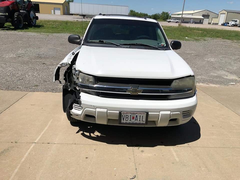 A white Chevrolet SUV parked on concrete with significant damage to the front passenger-side bumper and fender.