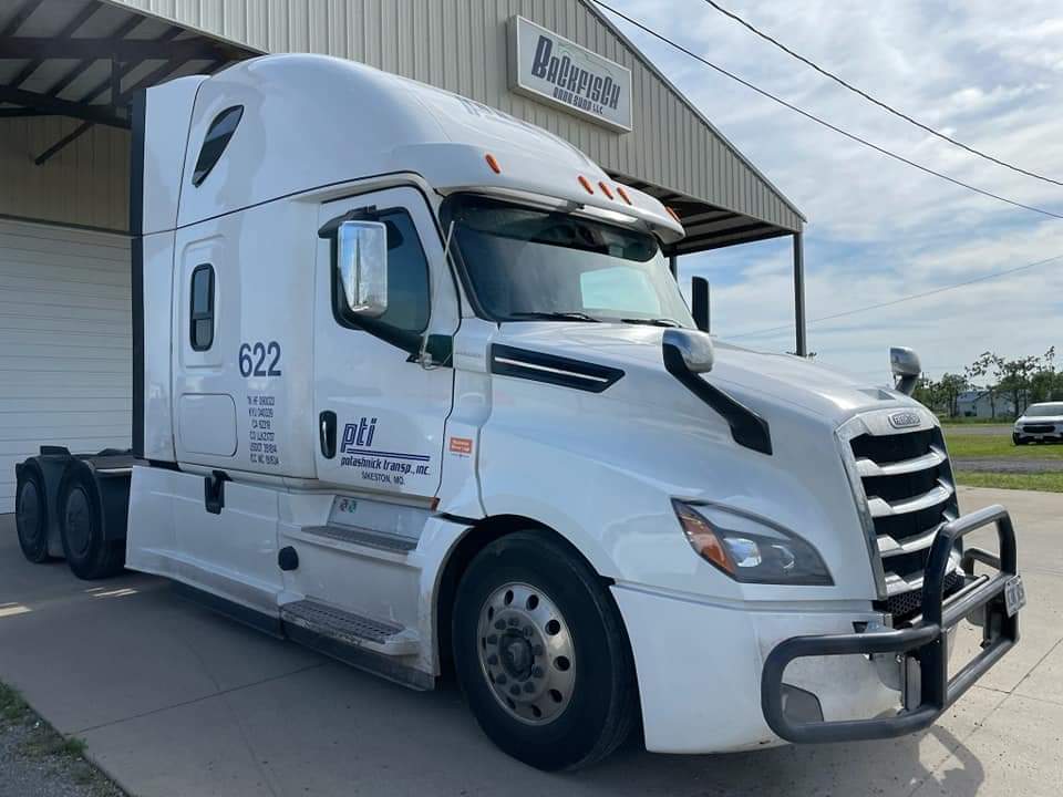 A white semi-truck parked in front of a building on a bright day.