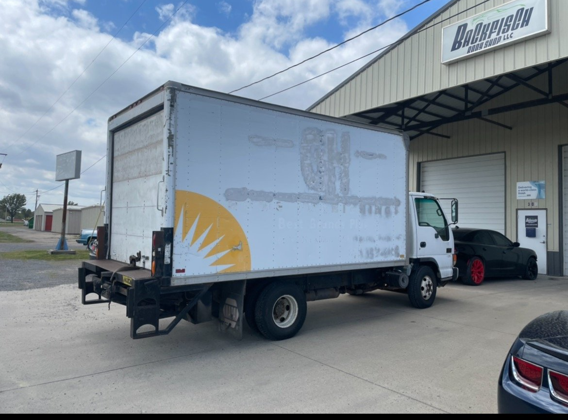 A white box truck parked in front of a commercial warehouse under a partly cloudy sky.