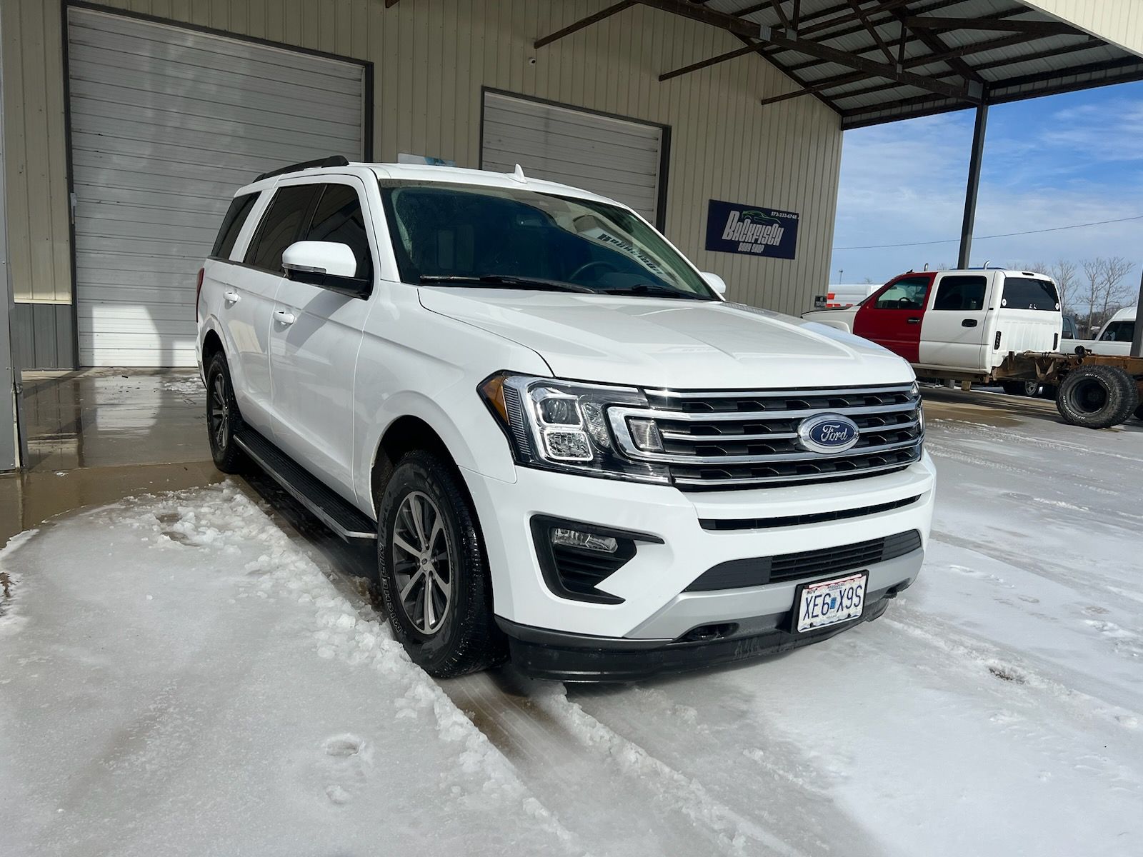 A white Ford Expedition parked on a snow-covered concrete lot in front of a building.