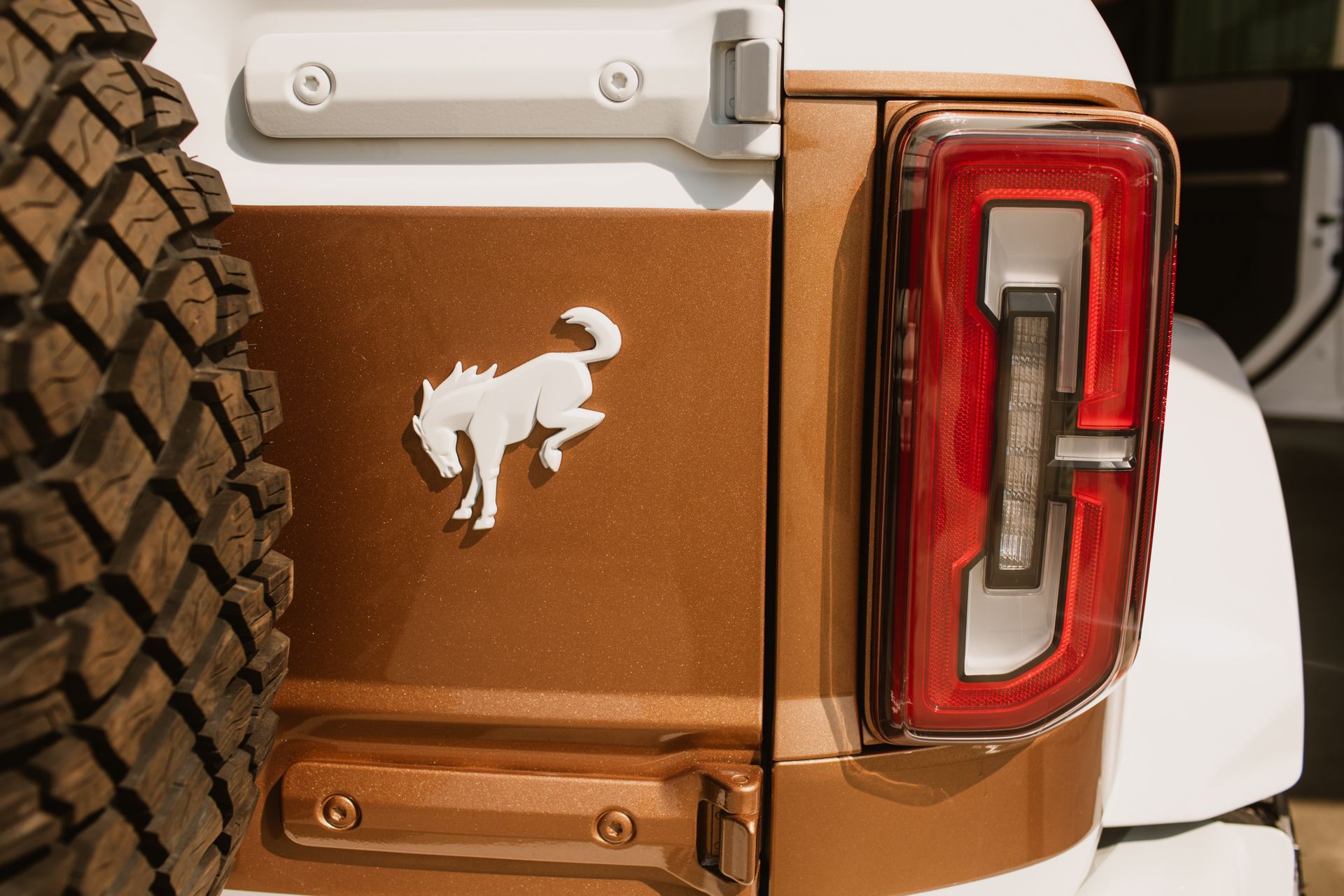 A metallic bronze Ford Bronco rear panel featuring a white bucking horse logo next to a red and clear vertical taillight.