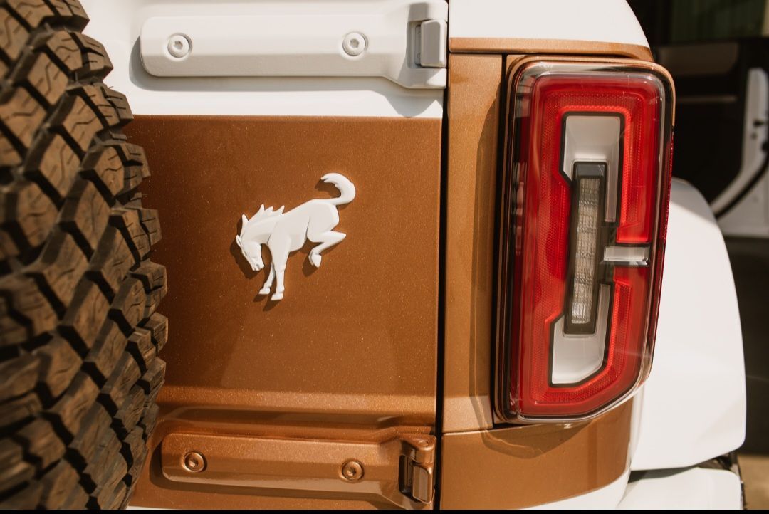 A close-up of a bronze Ford Bronco rear panel featuring a white bucking horse logo and a modern LED tail light.