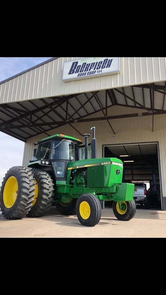 A green John Deere tractor with dual rear wheels parked in front of a shed with a 
