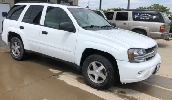 A white Chevrolet Trailblazer parked on a concrete lot next to a tan SUV.