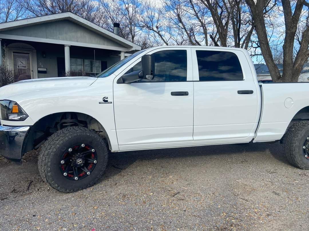 A white Ram crew cab pickup truck parked on a gravel driveway in front of a house.