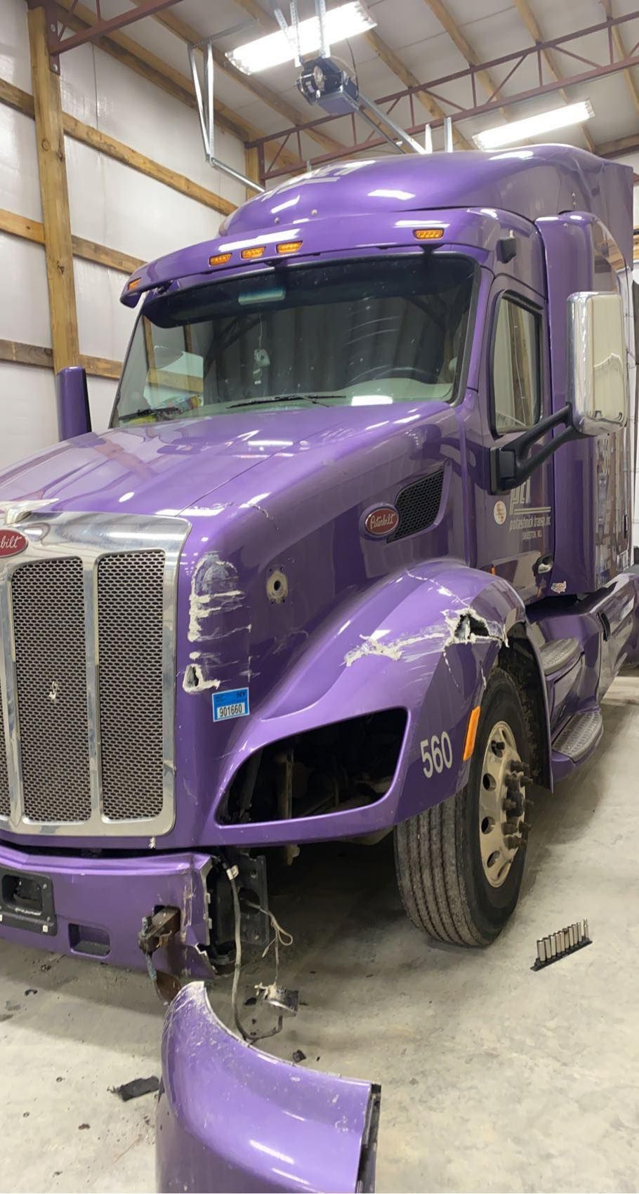 A damaged purple semi-truck parked inside a garage with its bumper partially detached.