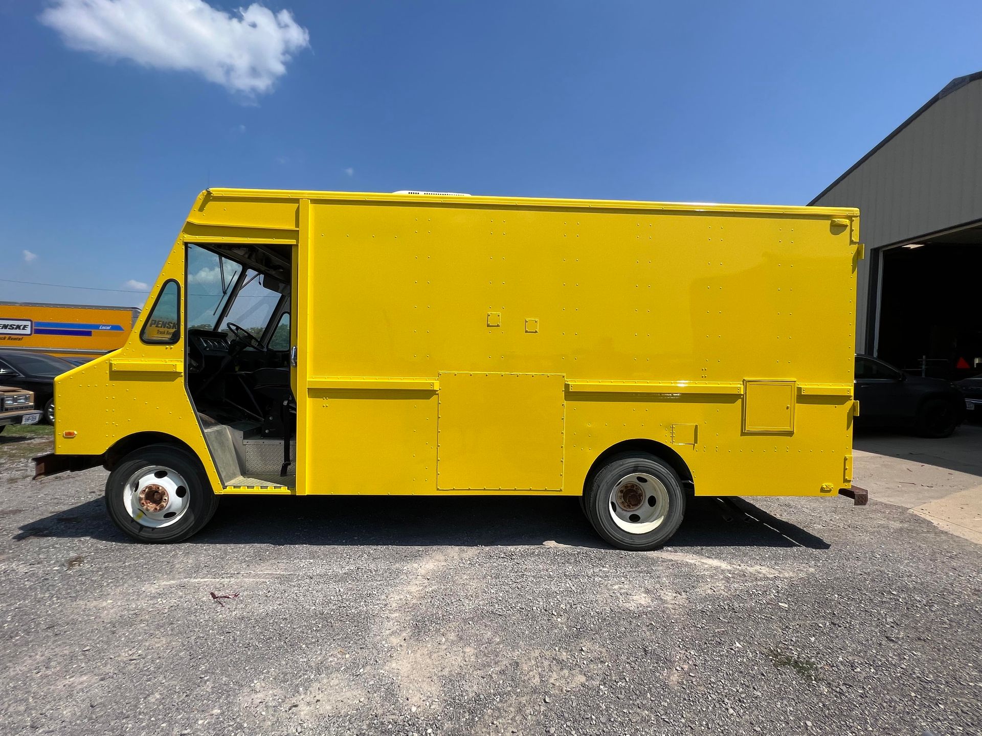A bright yellow step van parked on a gravel lot under a clear blue sky.