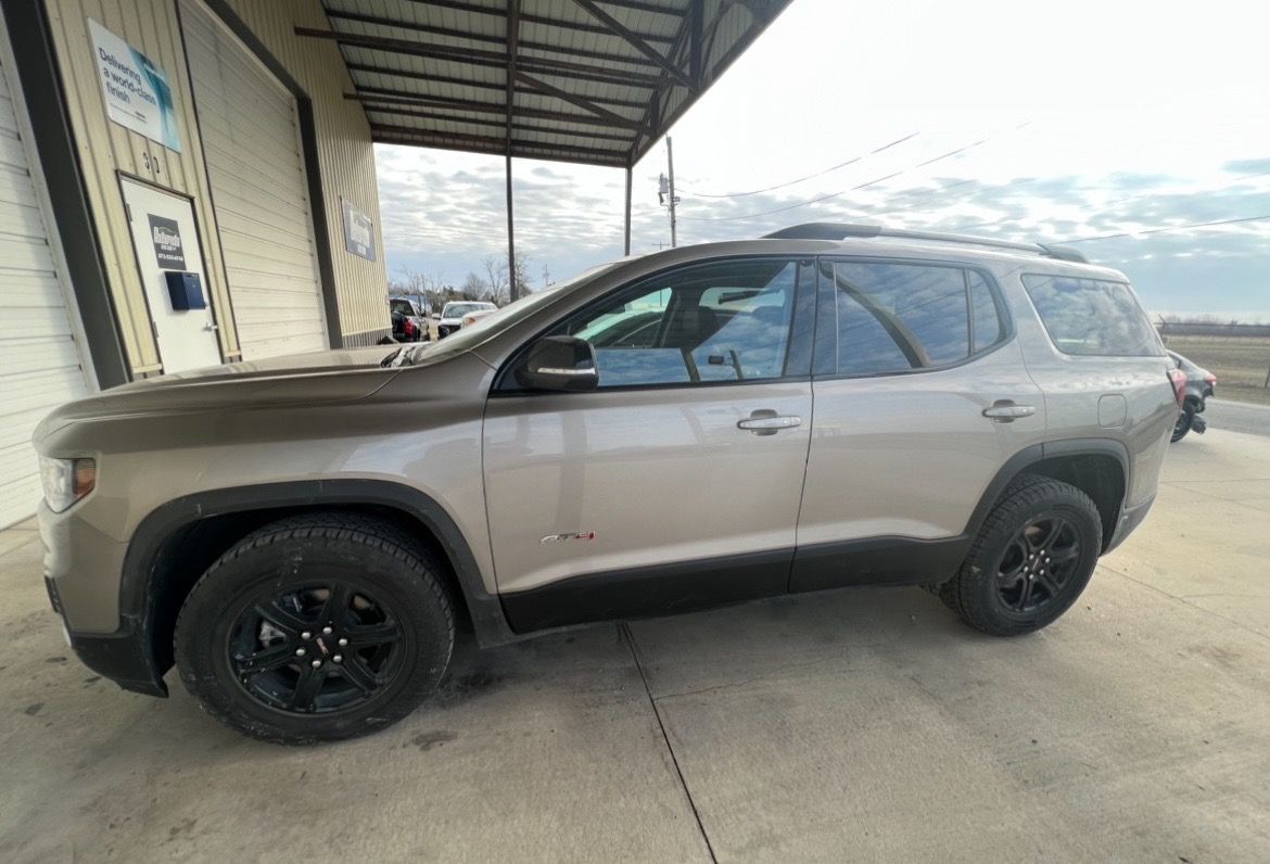 A tan Chevrolet Traverse SUV with black wheels parked on a concrete lot outside a building.