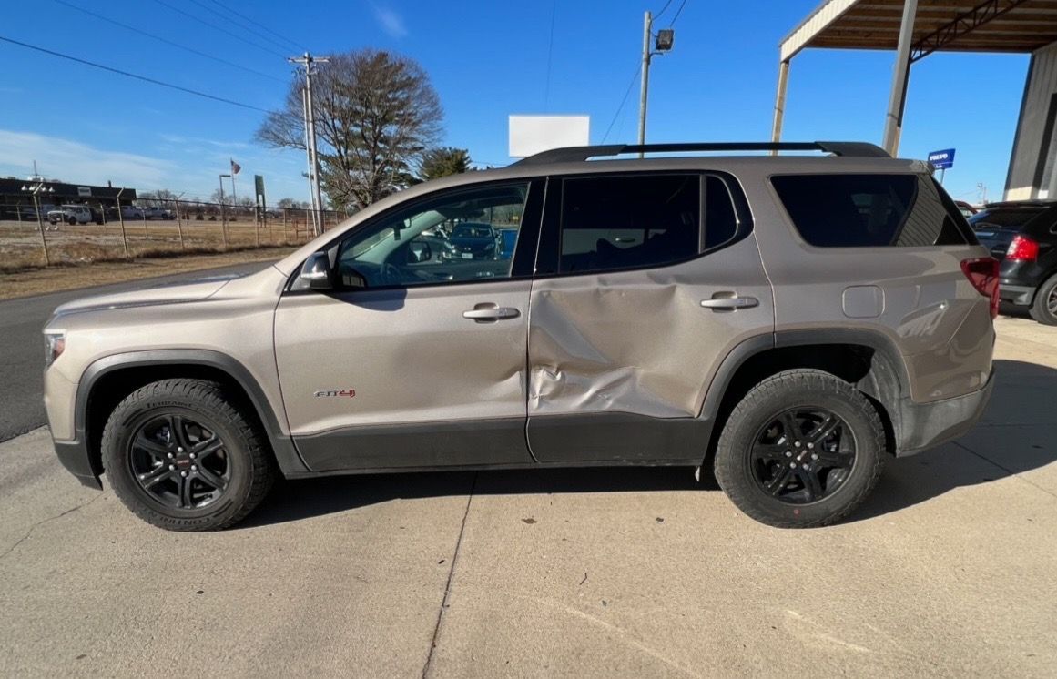 A tan SUV parked outdoors shows significant body damage and a large dent on the rear passenger-side door.
