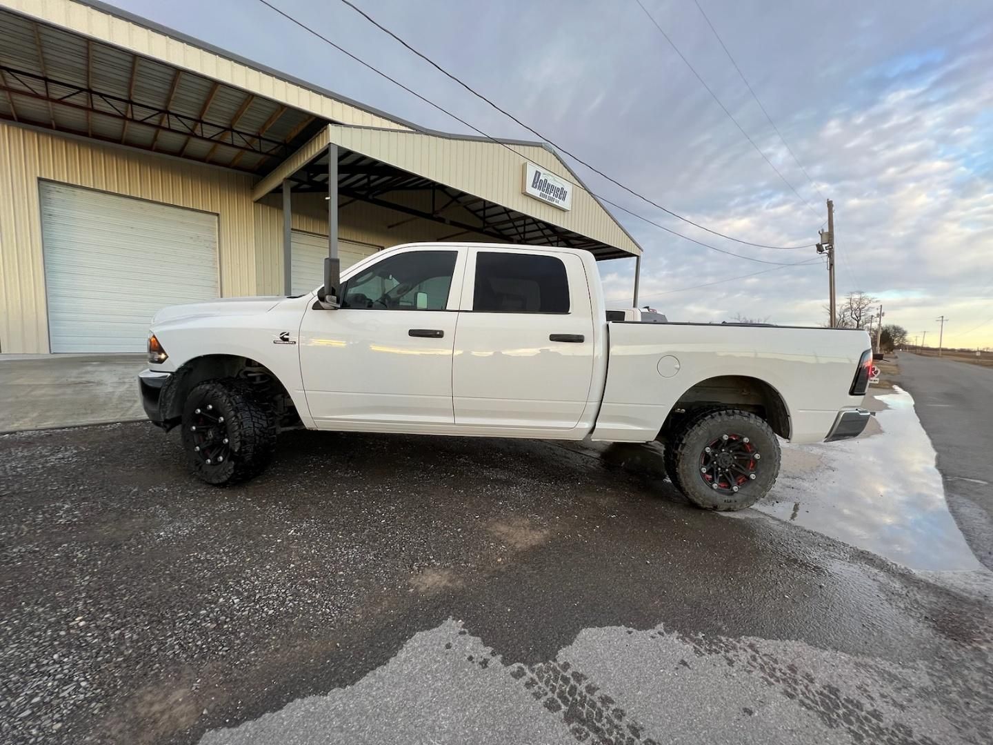 A white crew cab pickup truck parked on an asphalt lot in front of a metal commercial building under a cloudy sky.
