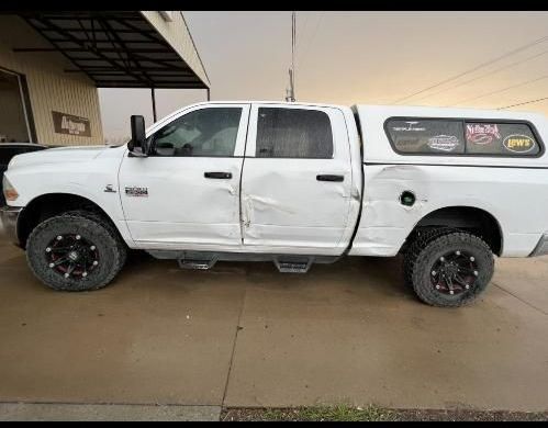 A white pickup truck parked on concrete, showing significant side-body collision damage along the doors and rear panel.