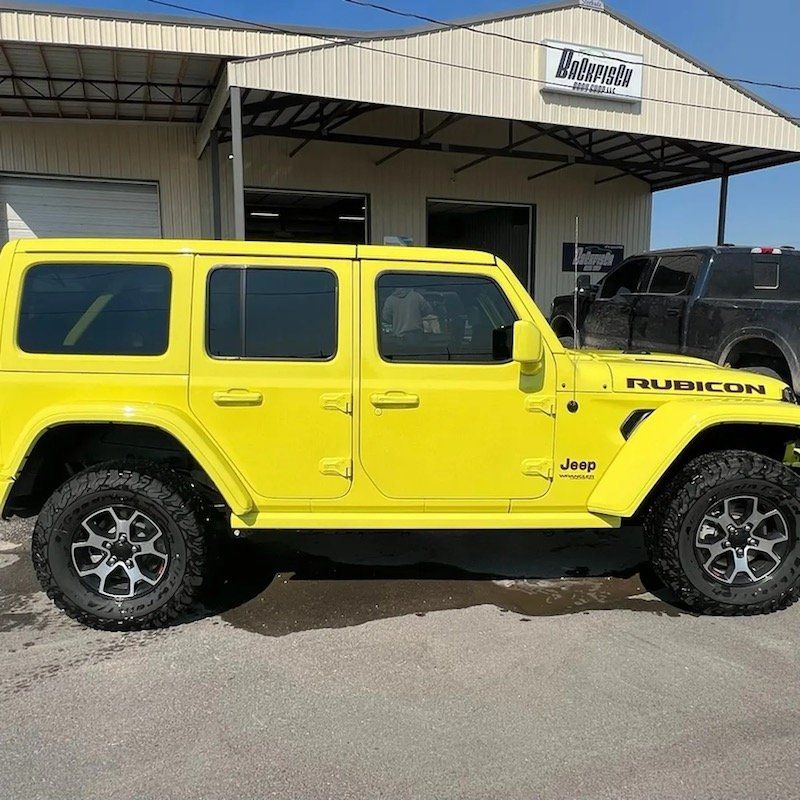 A bright yellow Jeep Wrangler Rubicon parked on a concrete lot in front of a building.