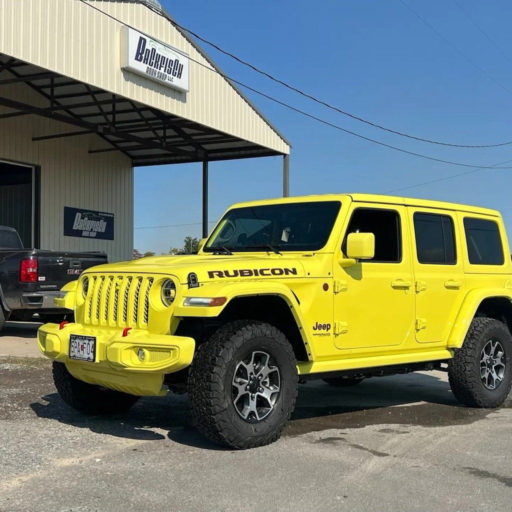 A bright yellow Jeep Wrangler Rubicon parked on a paved lot in front of a building with a metal roof.