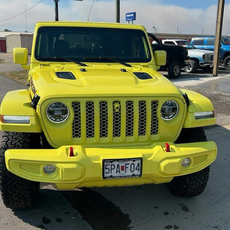 A bright yellow Jeep Wrangler parked on a lot, seen from the front view, with a visible license plate and off-road tires.