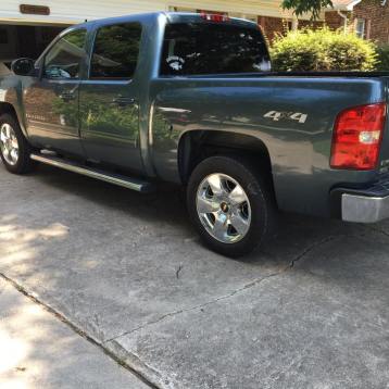 A blue crew cab 4x4 pickup truck parked on a concrete driveway in front of a house.