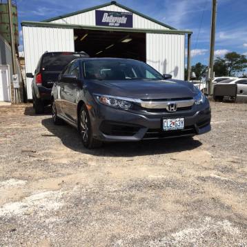 A dark gray Honda Civic parked on a gravel lot in front of a white metal-sided workshop building.