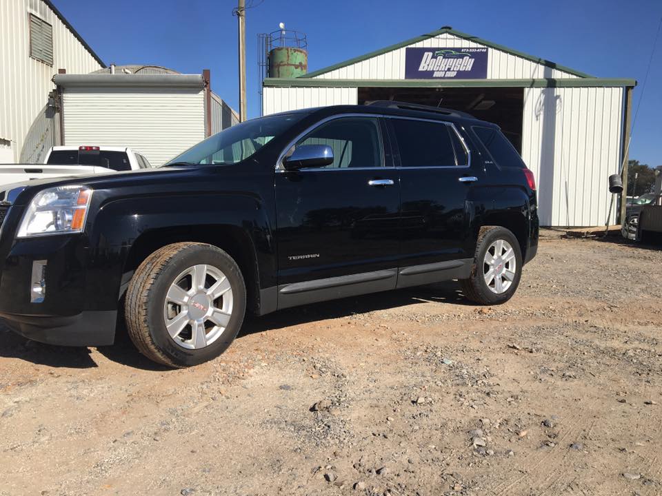 A black GMC Terrain SUV parked on a gravel lot in front of an industrial building.