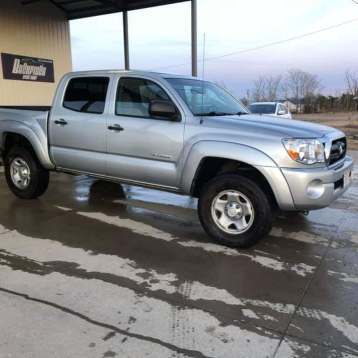 A silver Toyota Tacoma double cab pickup truck parked on a wet concrete surface under an open-sided structure.