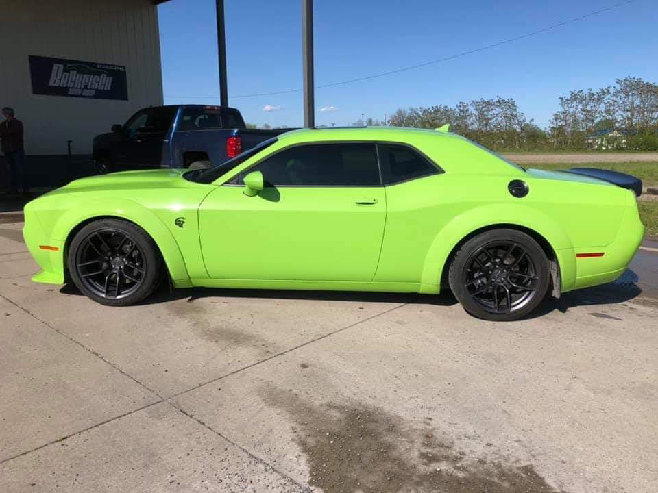 A lime-green Dodge Challenger widebody parked on a concrete lot on a sunny day.