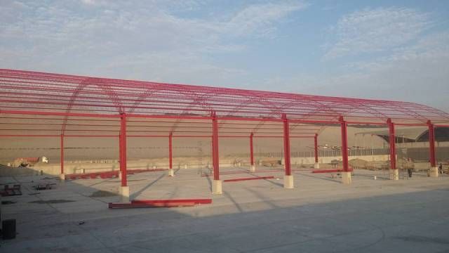 Estructura metálica roja tipo toldo sobre un terreno pavimentado en el desierto bajo un cielo azul.