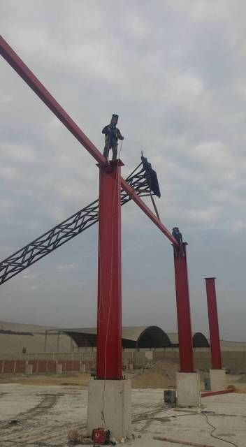 Obra en construcción con columnas de acero rojo y trabajadores en la parte superior bajo un cielo nublado.