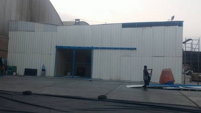 Exterior de un edificio industrial con revestimiento metálico blanco y una persona de pie en la azotea cerca de un equipo.