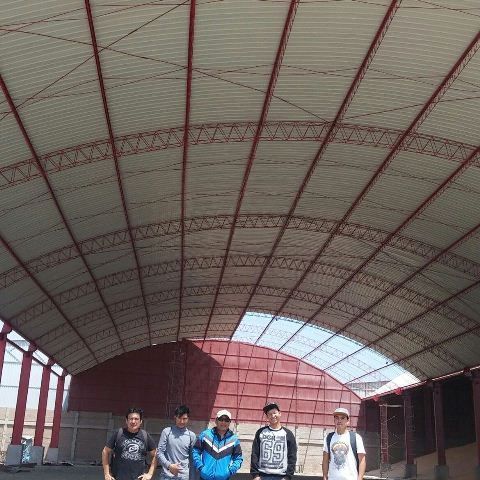 Cinco personas de pie bajo un gran pabellón arqueado con techo de metal y soportes rojos.