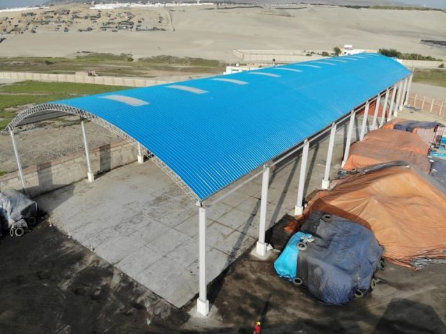 Refugio abierto con techo azul junto a equipo cubierto con lona en una zona rural al aire libre.