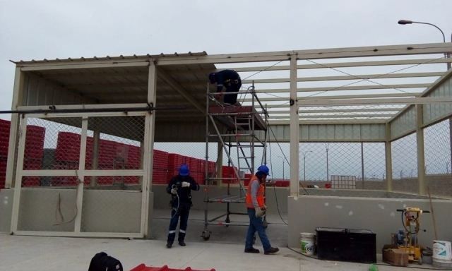 Obreros ensamblando una estructura metálica al borde de la carretera, con andamios y un techo parcialmente construido.
