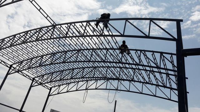 Dos trabajadores en la estructura de un techo de acero en construcción bajo un cielo nublado.