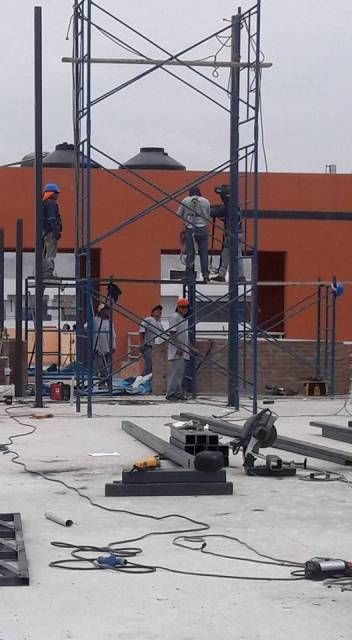 Obreros en andamios en una obra de construcción junto a una pared naranja.