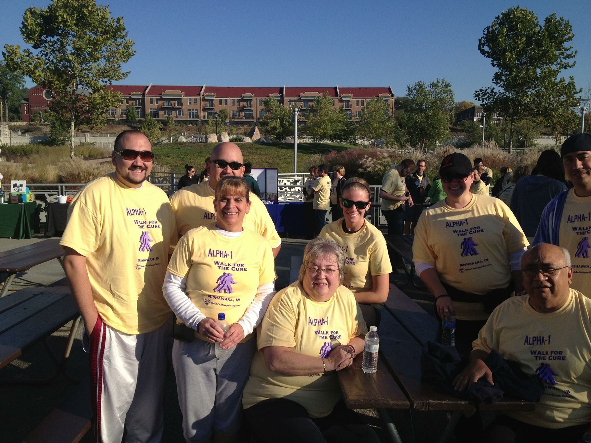Group of people in yellow shirts posing outdoors in a park on a sunny day