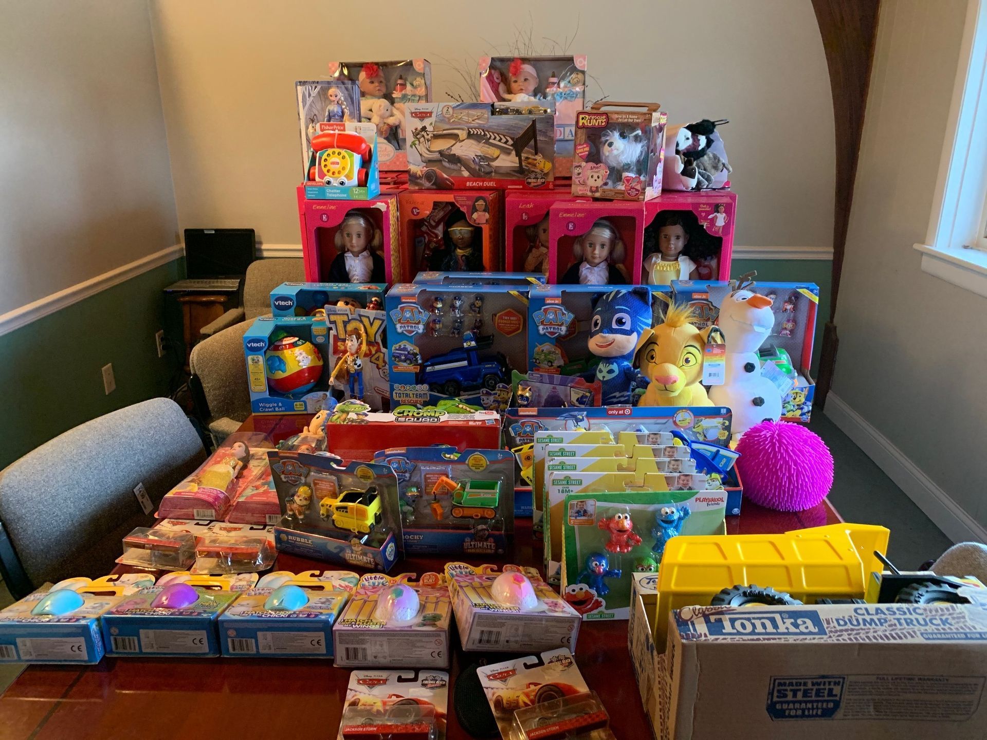 Table covered with colorful stacked toy and game boxes in a room with chairs and a window.