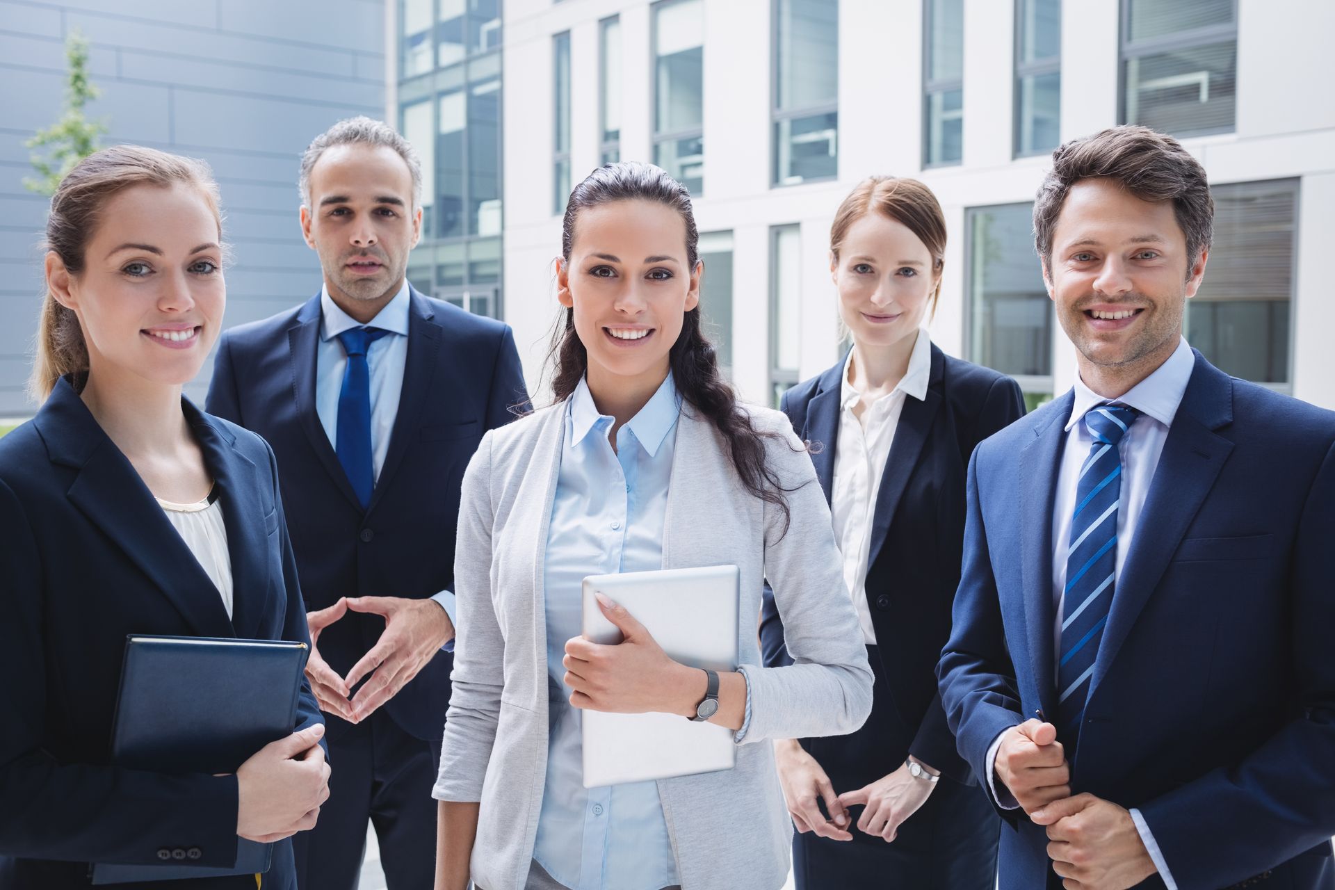 Five business professionals in suits standing outdoors in front of office buildings
