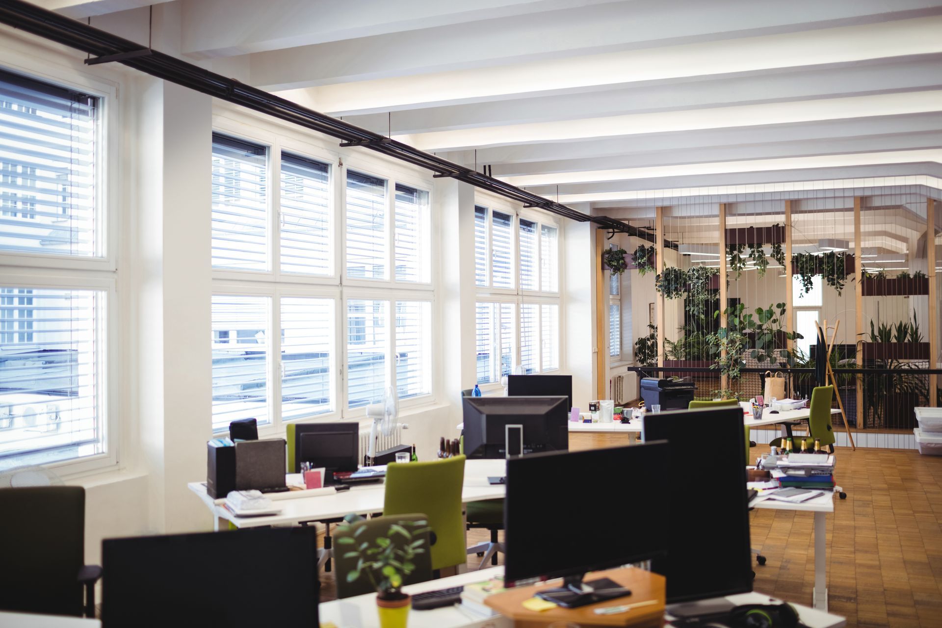 Bright open office with desks, computer monitors, and large windows letting in daylight.