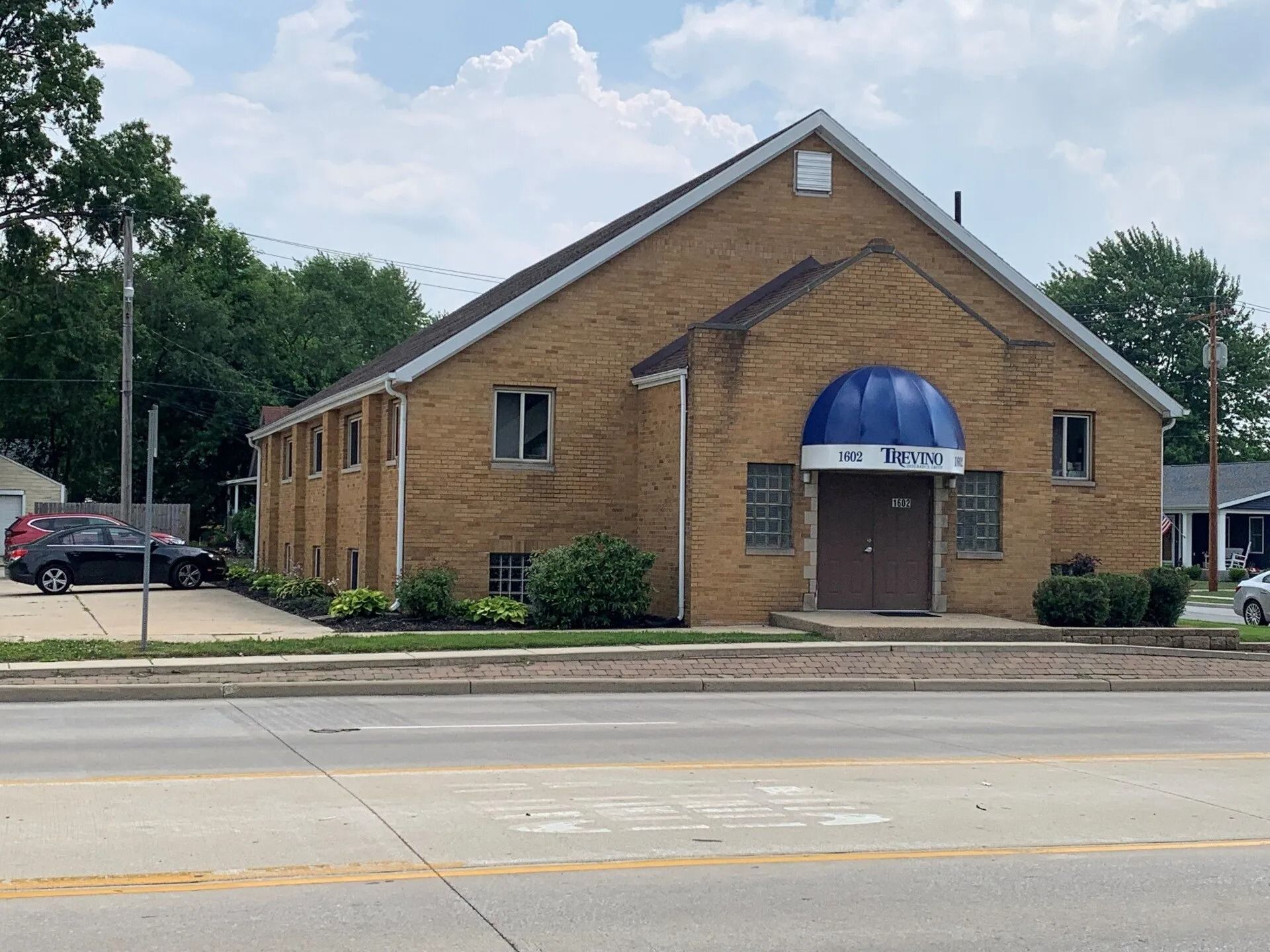 Brick church building with a blue awning beside a street under a cloudy sky