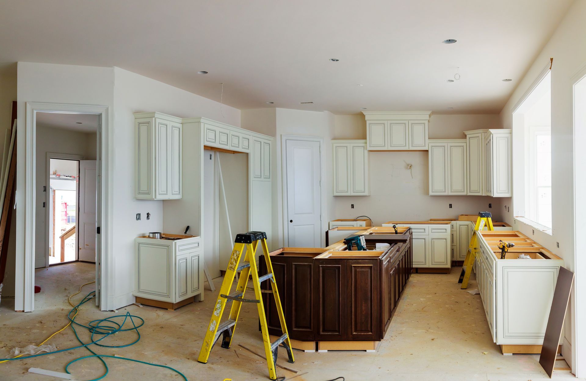 Kitchen under construction; white cabinets, brown island, yellow ladder, and tools.