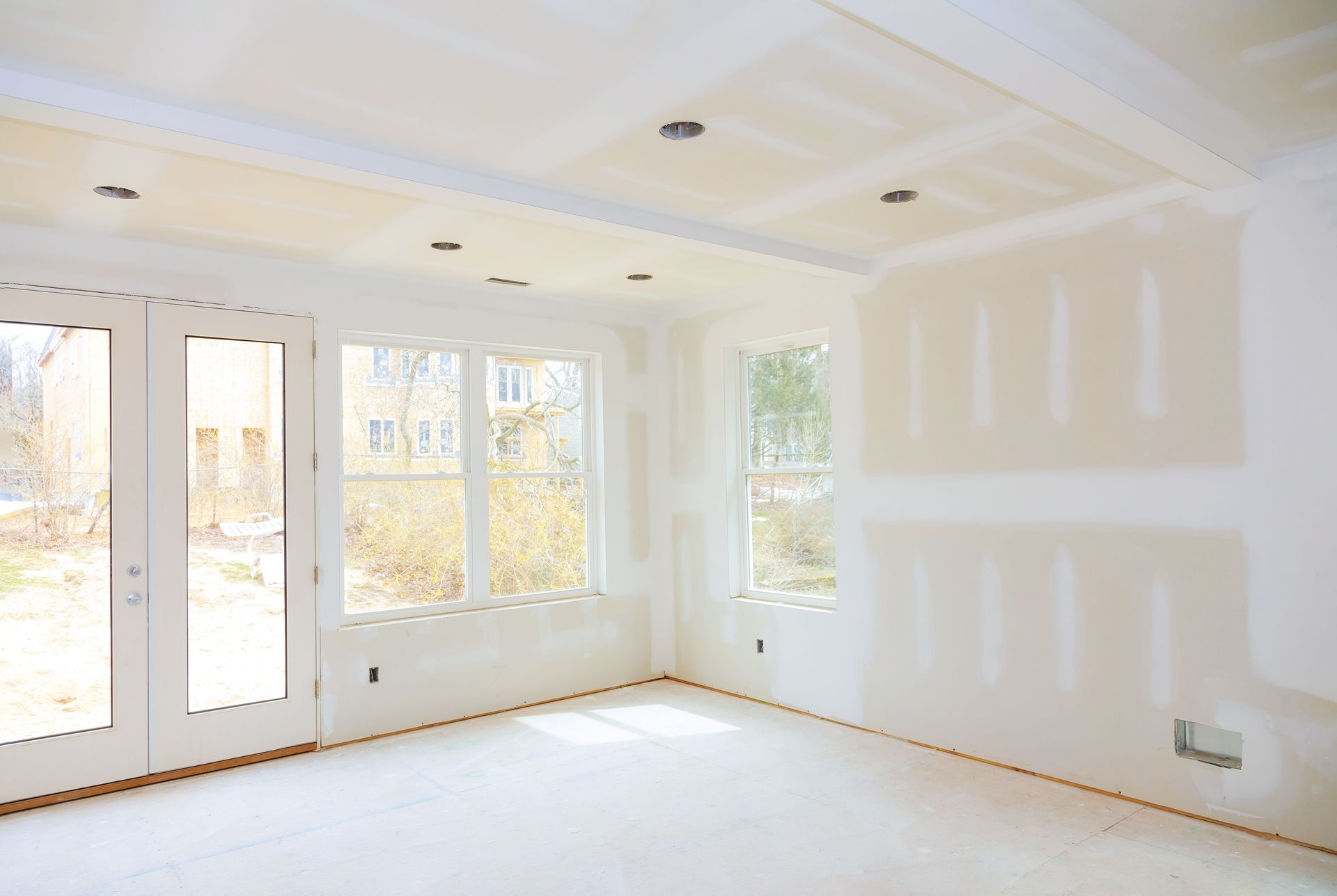 Interior room under construction, with drywall walls and ceiling, windows, and a doorway.
