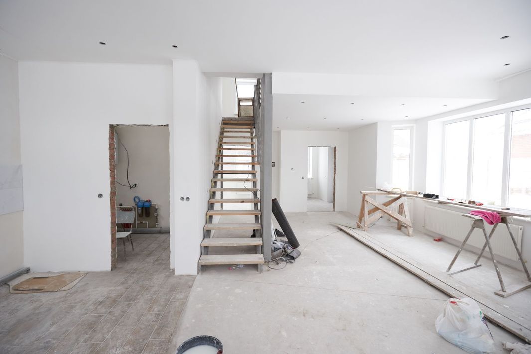Interior view of a building under renovation, featuring a wooden staircase, bare walls, and construction materials.