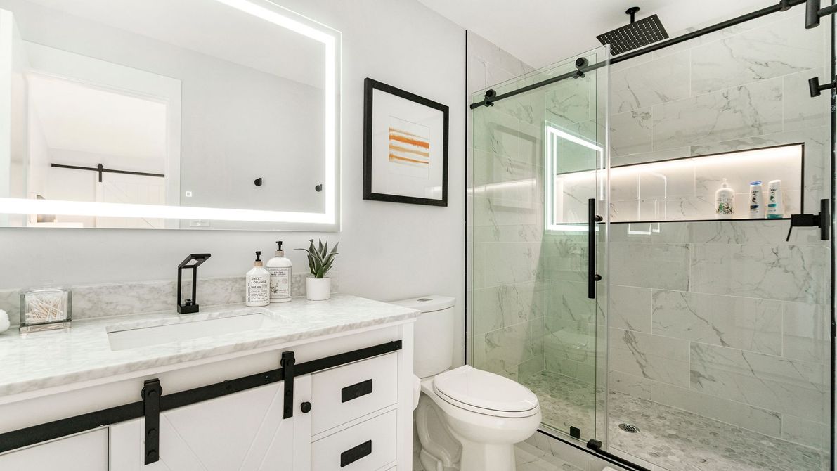 Modern bathroom with white vanity, black hardware, glass shower, and illuminated mirror.