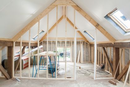 Interior view of a room under construction with exposed wooden beams, studs, and skylights.