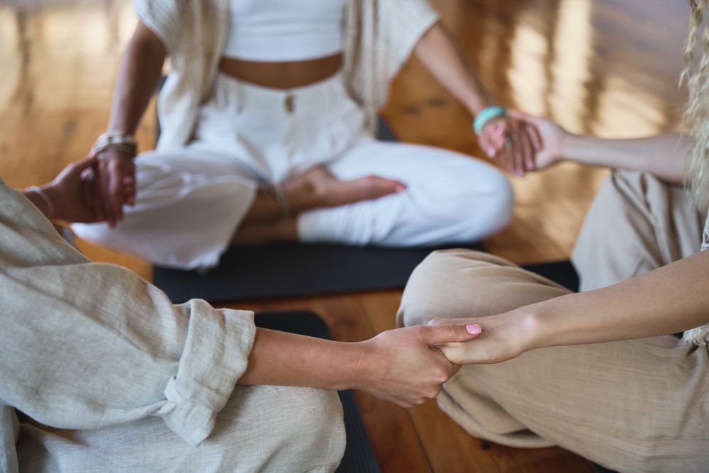 A group of people are sitting in a circle on a yoga mat holding hands.