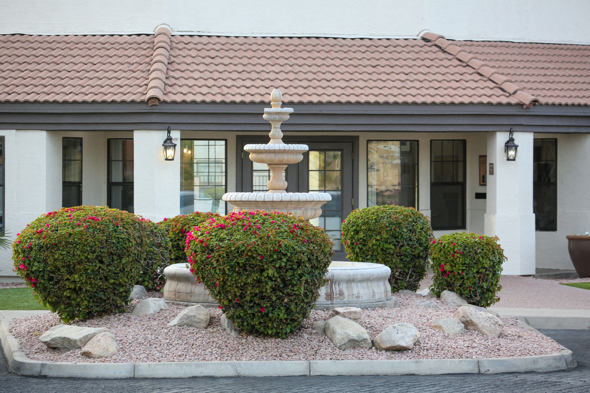 Front yard fountain surrounded by trimmed shrubs in front of a single-story house