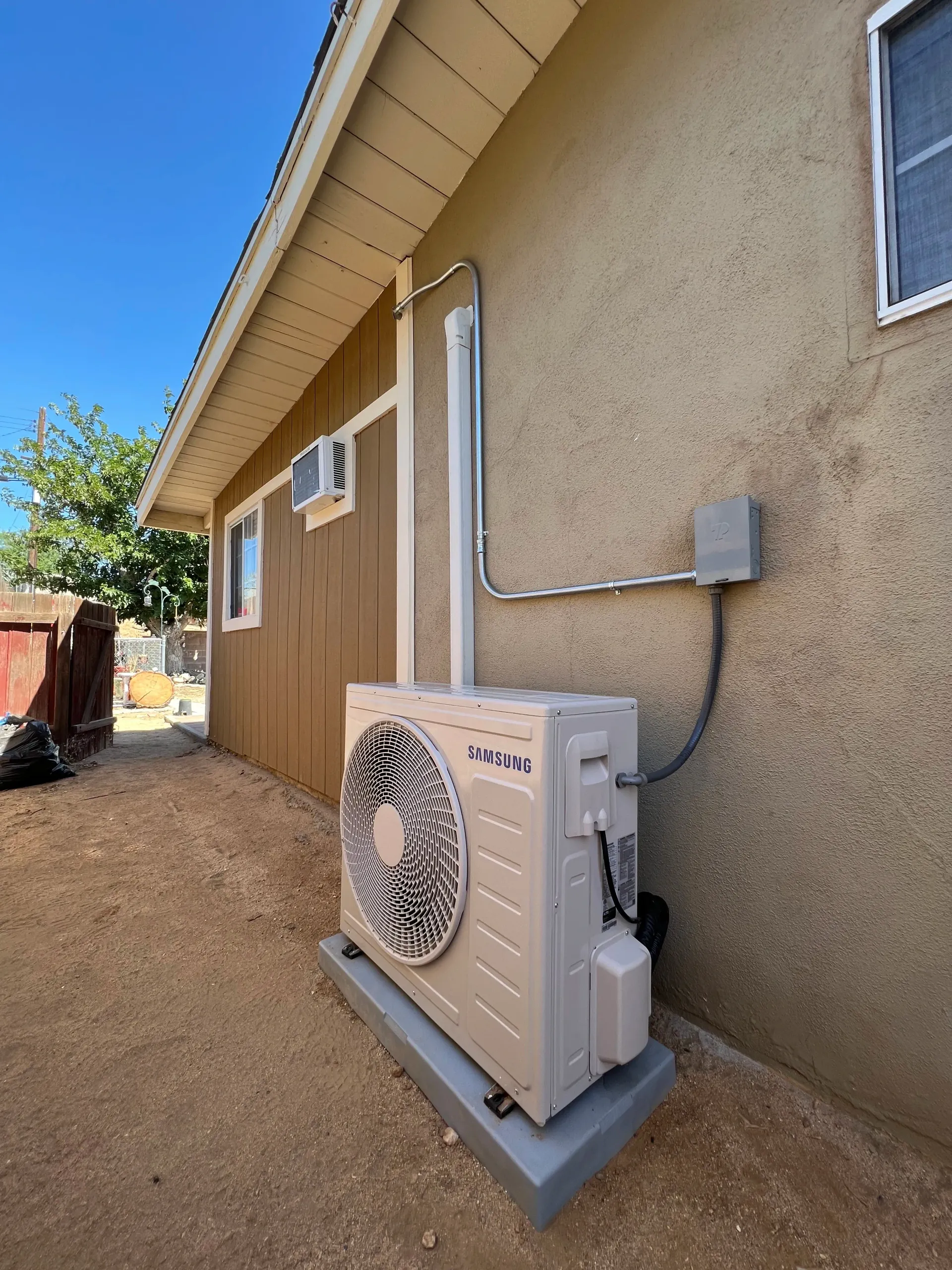 Outdoor HVAC mini-split unit beside beige house exterior on gravel ground