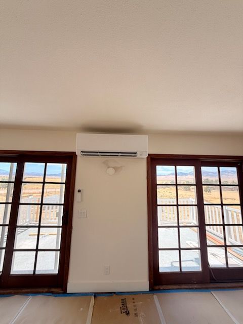 Empty room with wall-mounted air conditioner between two large wood-framed glass doors.
