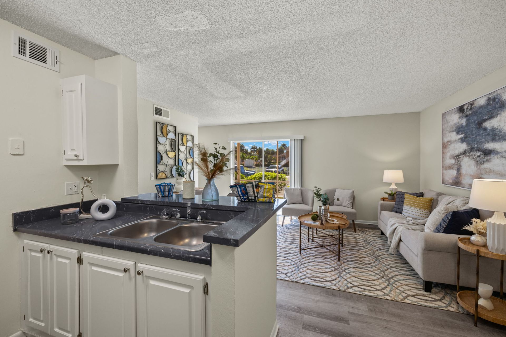 A kitchen area opens to a living room with a sofa, rug, and balcony.
